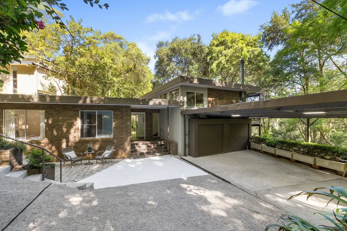 Exterior of a brick house with a covered double garage, paved courtyard and surrounding trees