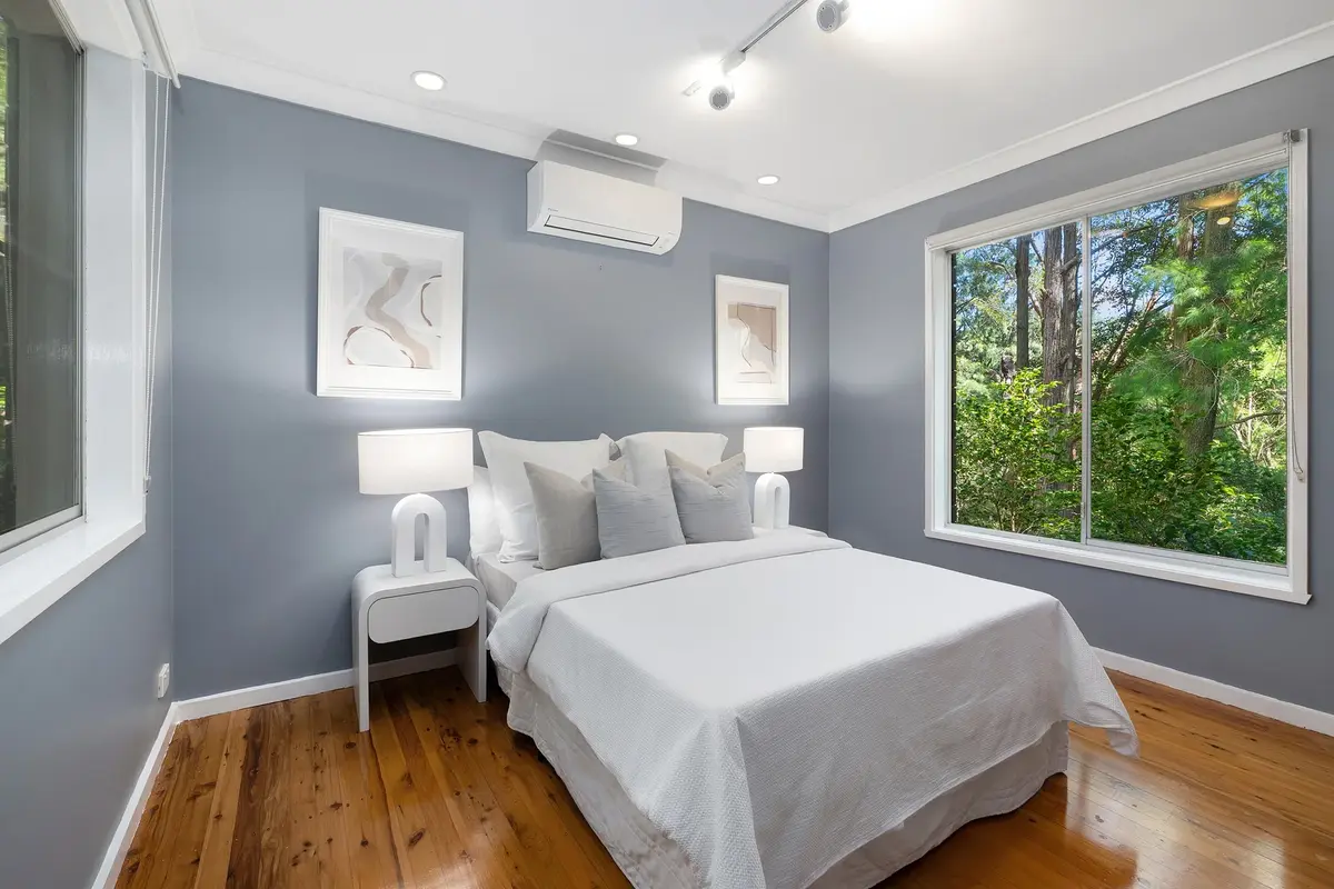 Bedroom with a white bed, grey walls, timber flooring and a large window overlooking trees.
