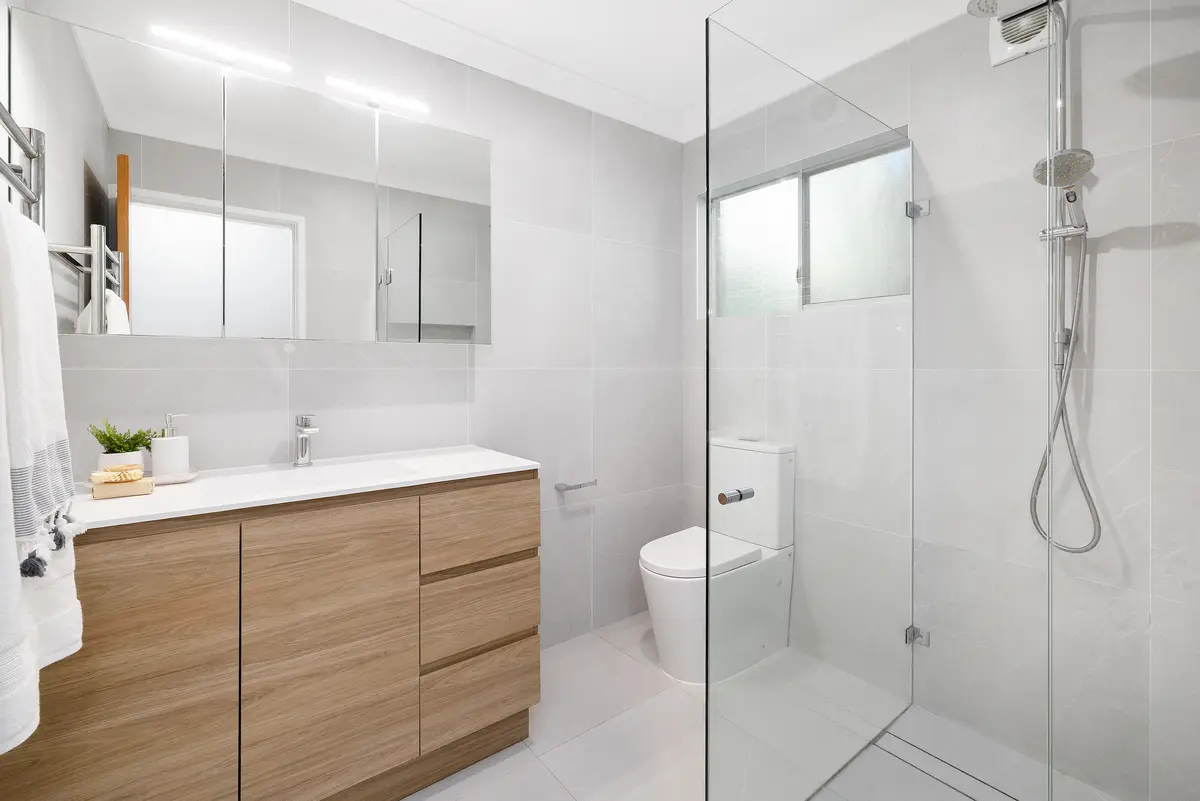 Bathroom with grey large-format tiles, a frameless glass shower with a rail shower, a toilet, and a timber-look vanity with a mirrored cabinet above