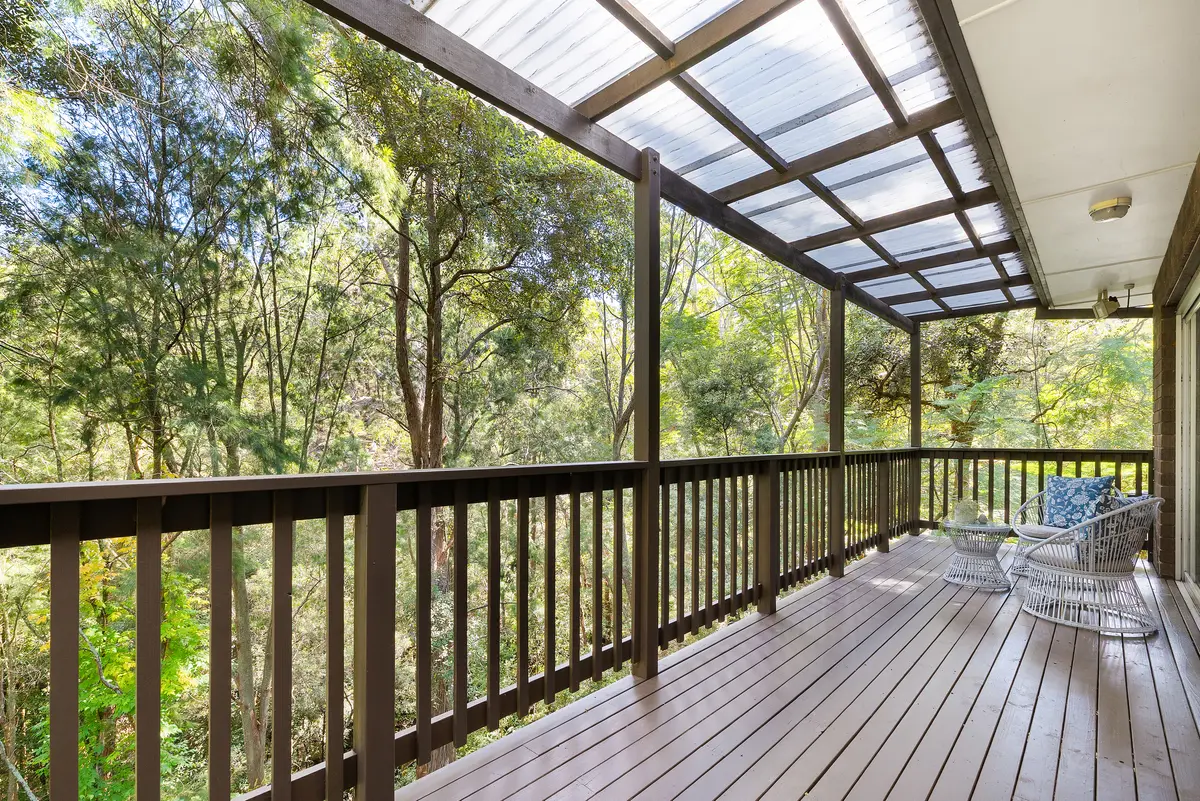 Covered timber deck with outdoor chairs and table overlooking dense trees.