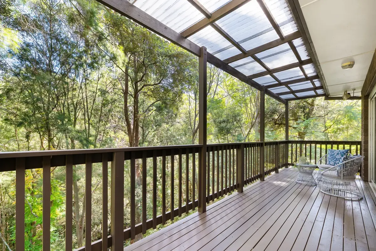 Covered timber deck with two chairs and a small table overlooking trees