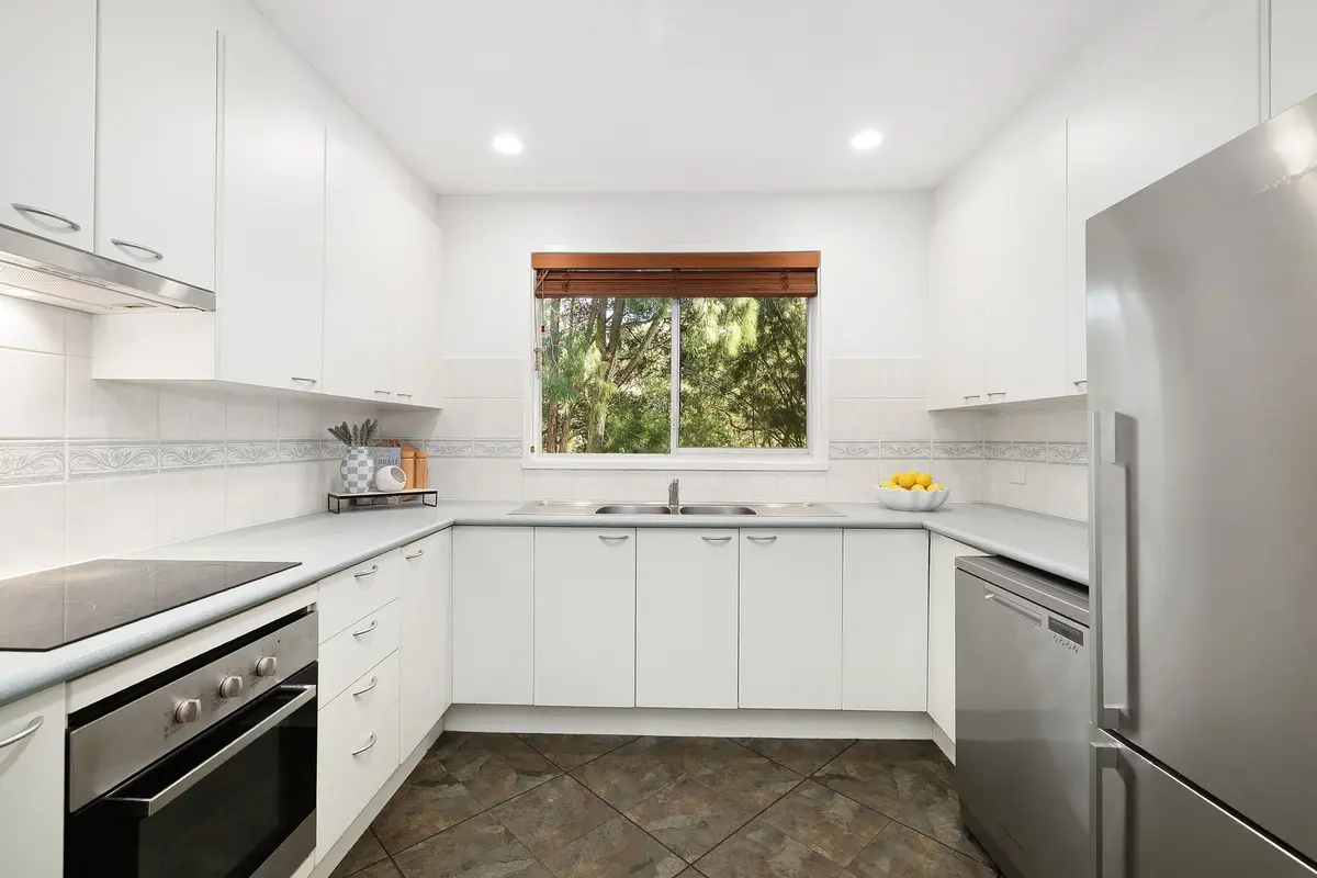 White U-shaped kitchen with stainless steel appliances and a window overlooking trees.