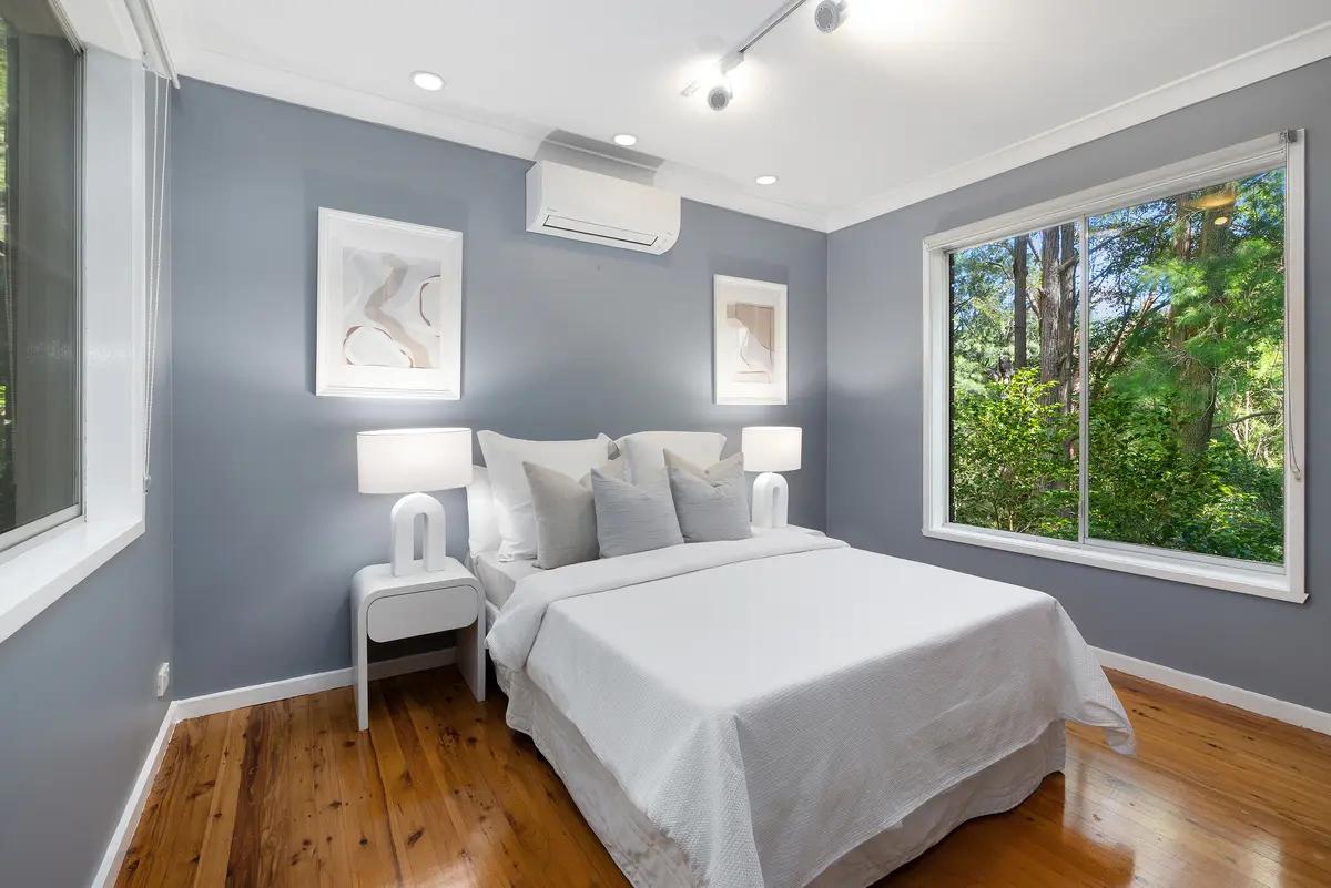 Light-filled bedroom with a neatly made bed, timber floors and a window looking onto trees