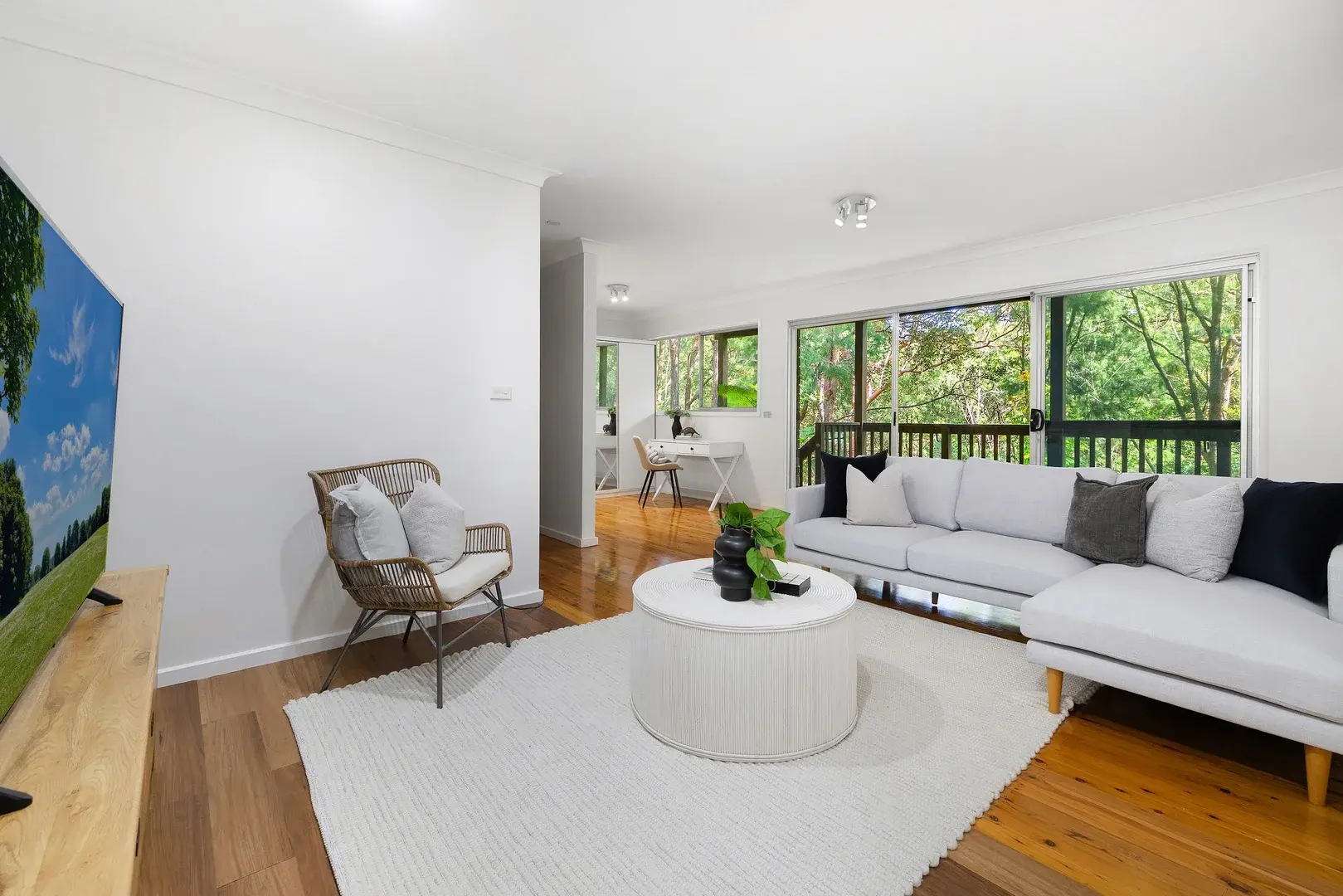 Living room with a pale corner sofa, timber floors and sliding doors overlooking trees.